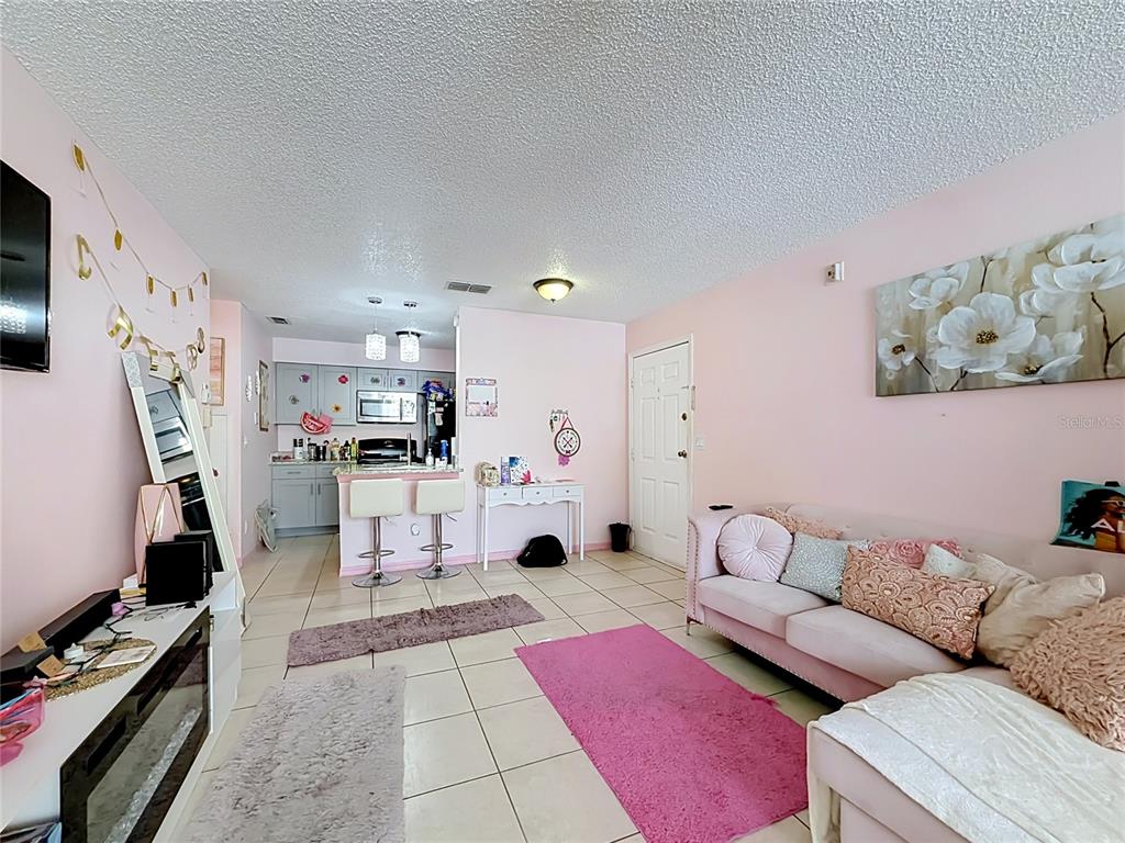 A living room with pink walls, tile flooring, and an open kitchen with bar seating — 1081 HIAWASSEE UNIT 713, ORLANDO, FL