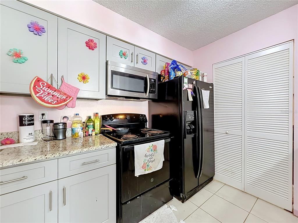 A kitchen features light gray cabinets, black appliances, granite countertops, and pink walls — 1081 HIAWASSEE UNIT 713, ORLANDO, FL