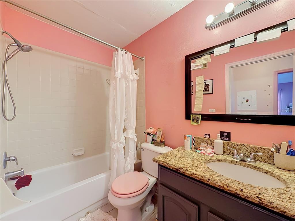 A bathroom features pink walls, a granite vanity, a dark cabinet, and a shower-tub combo — 1081 HIAWASSEE UNIT 713, ORLANDO, FL