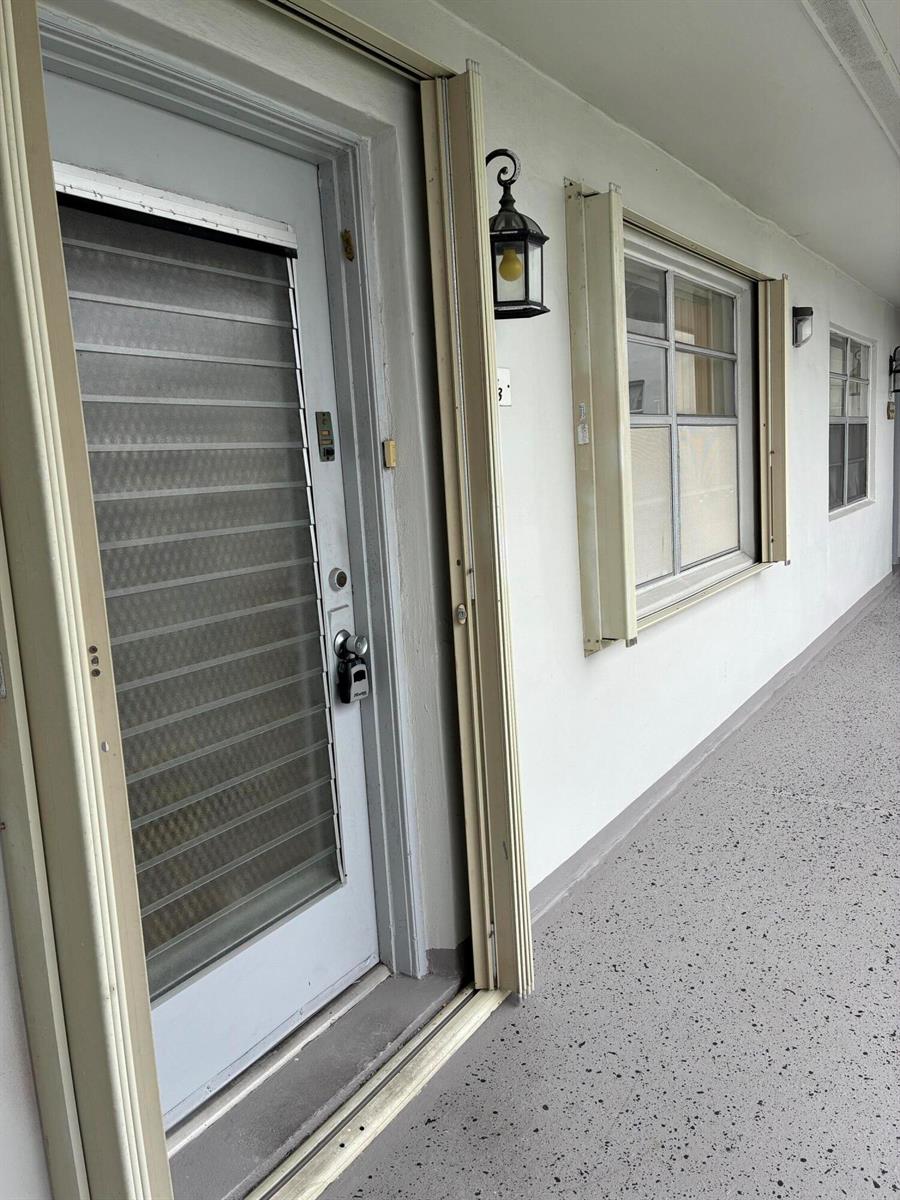 An exterior view of a building entrance featuring a white door with a security lock — 574 Burgundy L # 574, Delray Beach FL 33484, DELRAY BEACH, FL