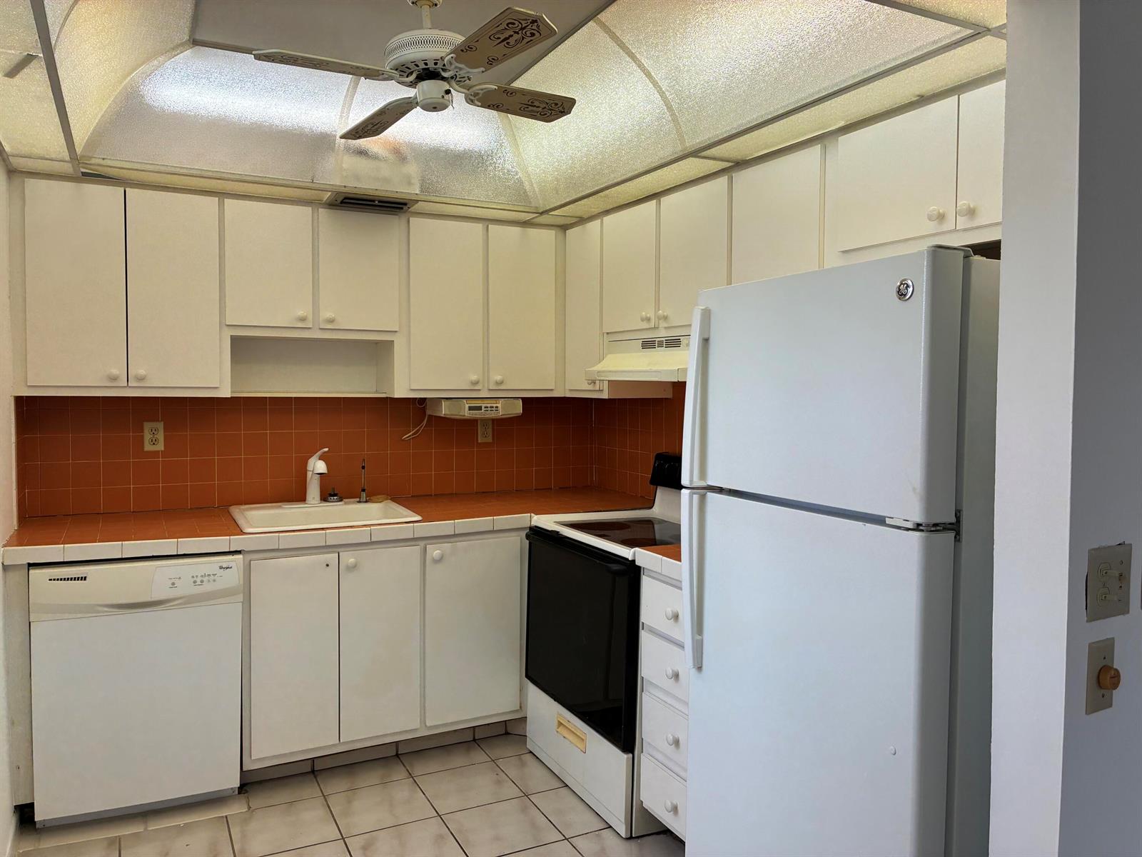 A kitchen with white cabinets, orange tile backsplash, white appliances, and a textured ceiling light — 574 Burgundy L # 574, Delray Beach FL 33484, DELRAY BEACH, FL