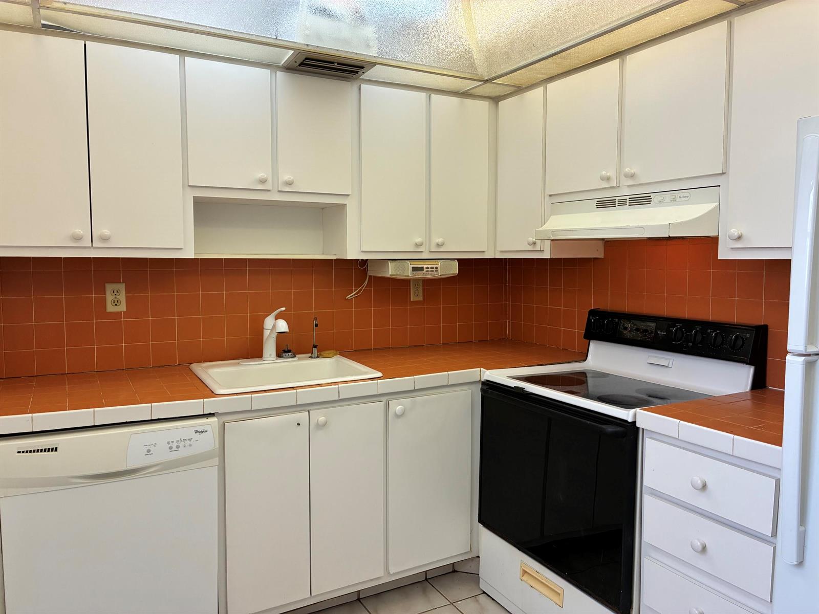 A kitchen features white cabinets, orange tiled countertops and backsplash, and black and white appliances — 574 Burgundy L # 574, Delray Beach FL 33484, DELRAY BEACH, FL