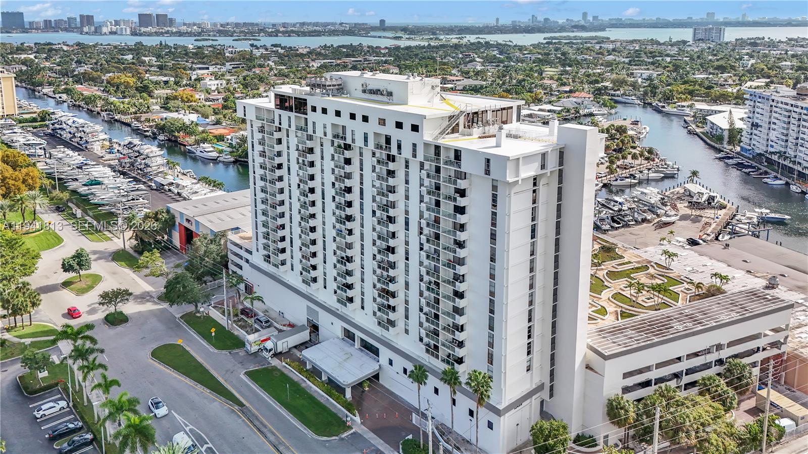 An aerial view shows a tall white residential building surrounded by canals and boat slips — 13499 Biscayne Blvd # 3, North Miami FL 33181, NORTH MIAMI, FL