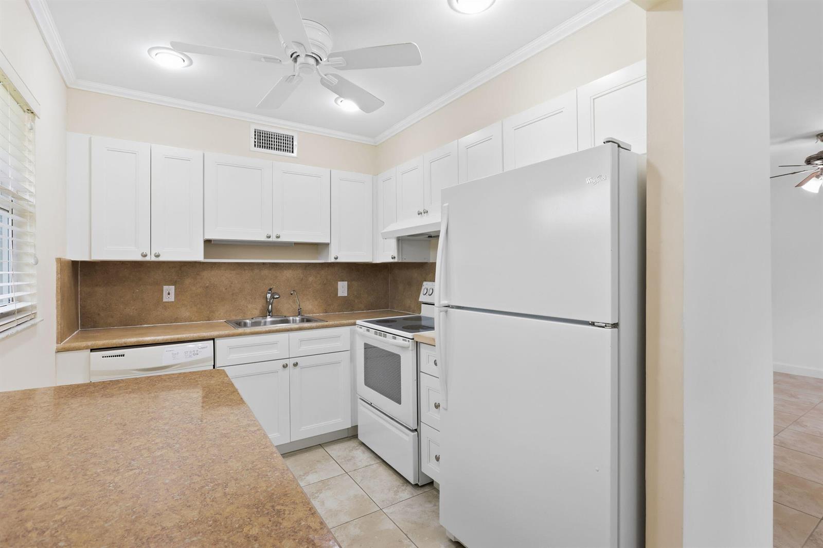 A kitchen features white cabinets, white appliances, a tan countertop, and light-colored tile flooring — 164 Seville G, Delray Beach FL 33446, DELRAY BEACH, FL
