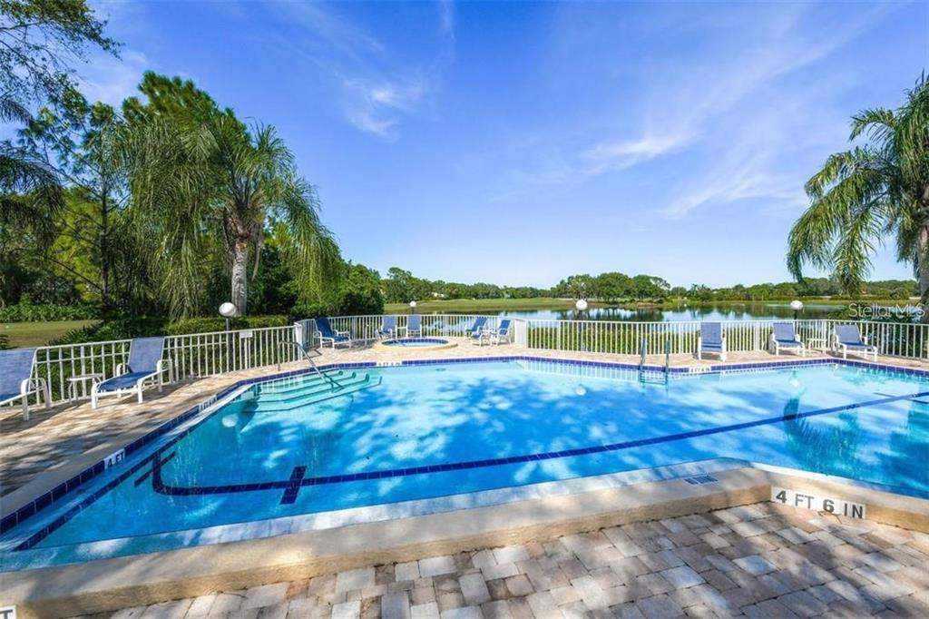 A swimming pool and hot tub overlook a lake with a white fence — 7904 HAMPTON COURT, UNIVERSITY PARK, FL