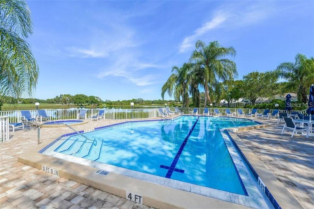 An outdoor swimming pool with a hot tub and lounge chairs overlooks a lake — 7904 HAMPTON COURT, UNIVERSITY PARK, FL