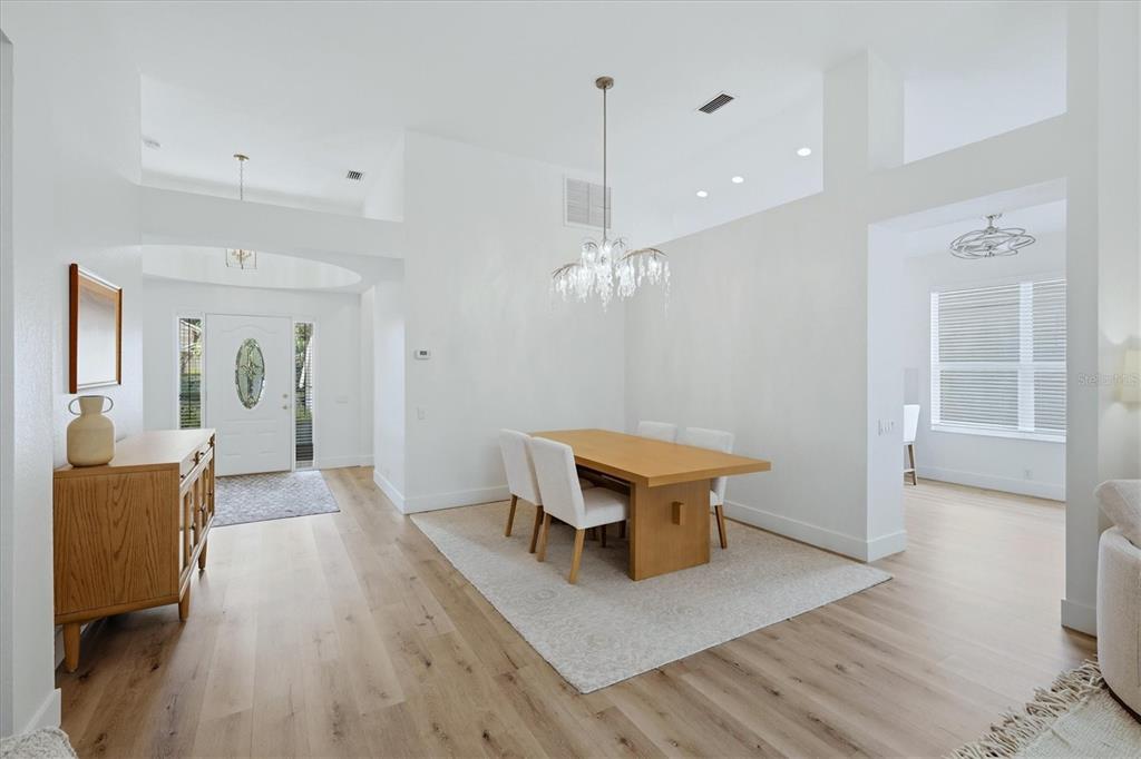 A dining area with a wooden table, chandelier, and light wood flooring near an entryway — 7904 HAMPTON COURT, UNIVERSITY PARK, FL