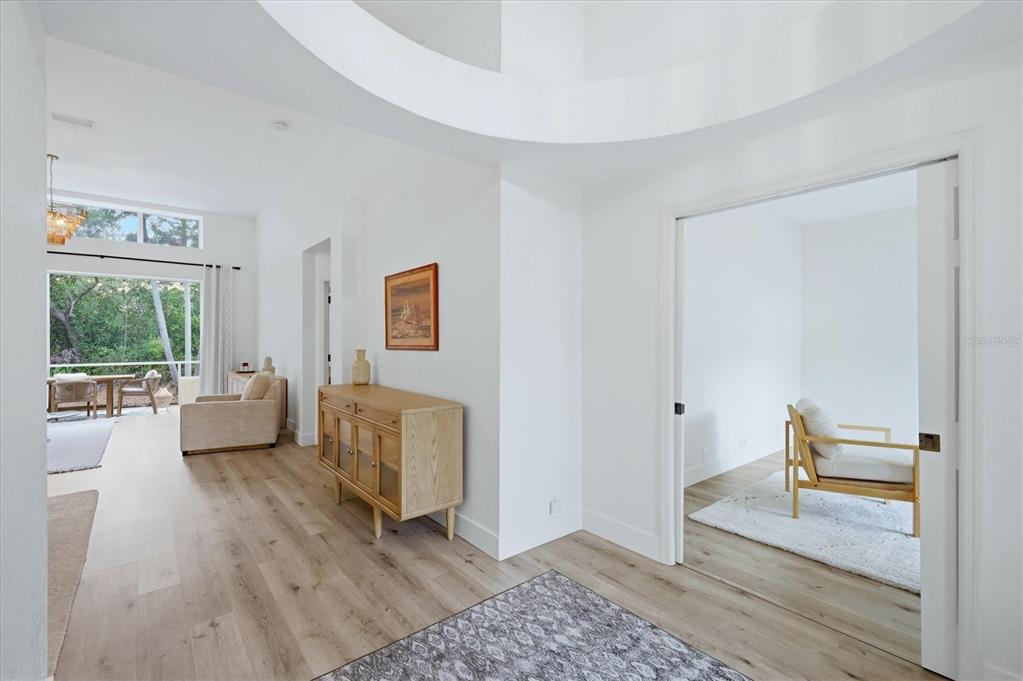 A bright hallway with light wood floors leads to a living area and a side room — 7904 HAMPTON COURT, UNIVERSITY PARK, FL