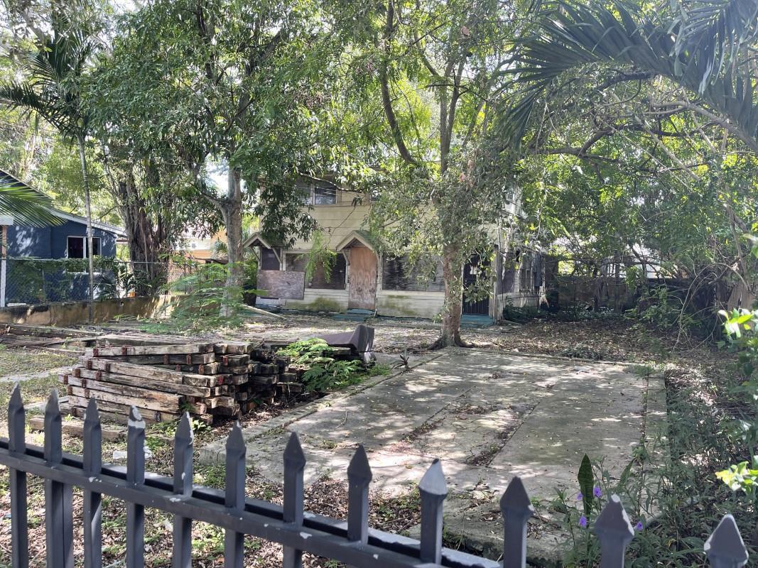 A two-story house with boarded-up windows sits behind a metal fence and stacked wooden beams — 252 NE 57th Street, Miami FL 33137, MIAMI, FL