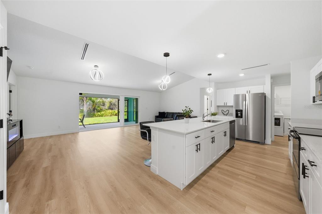 A bright, open-concept kitchen and living area features white cabinetry, a large island, and light wood-look flooring — 49 TROUTDALE STREET, PORT CHARLOTTE, FL