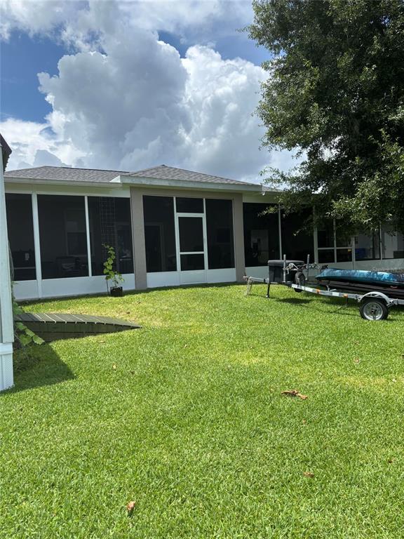 A backyard view of a house with a screened-in porch and a boat on a trailer — 121 DAISY LANE, LAKE PLACID, FL