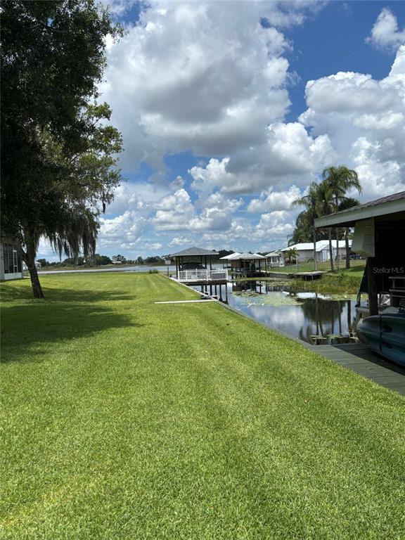 A grassy backyard leads to a canal with boat docks under a cloudy blue sky — 121 DAISY LANE, LAKE PLACID, FL