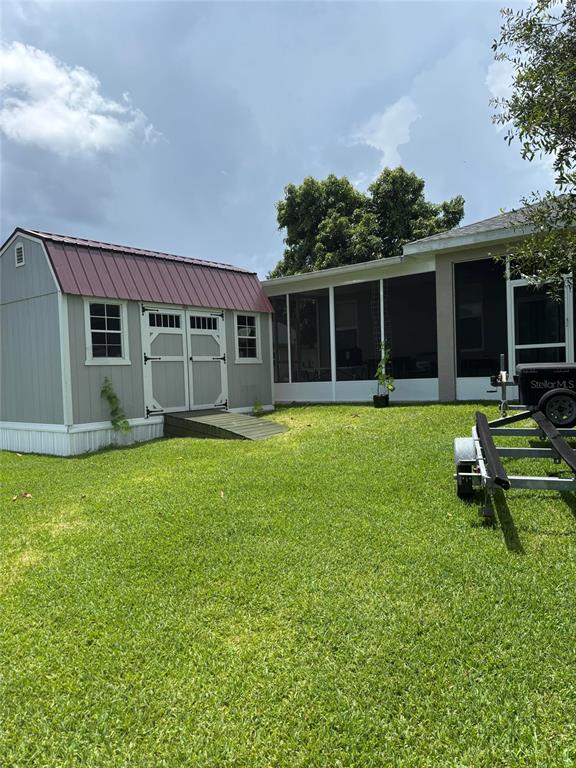 A backyard features a grey shed with a red roof, a screened-in porch, and a trailer — 121 DAISY LANE, LAKE PLACID, FL