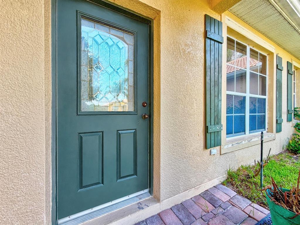 A dark green front door with a glass insert sits beside a window with shutters — 3505 FOREST PARK DRIVE, KISSIMMEE, FL