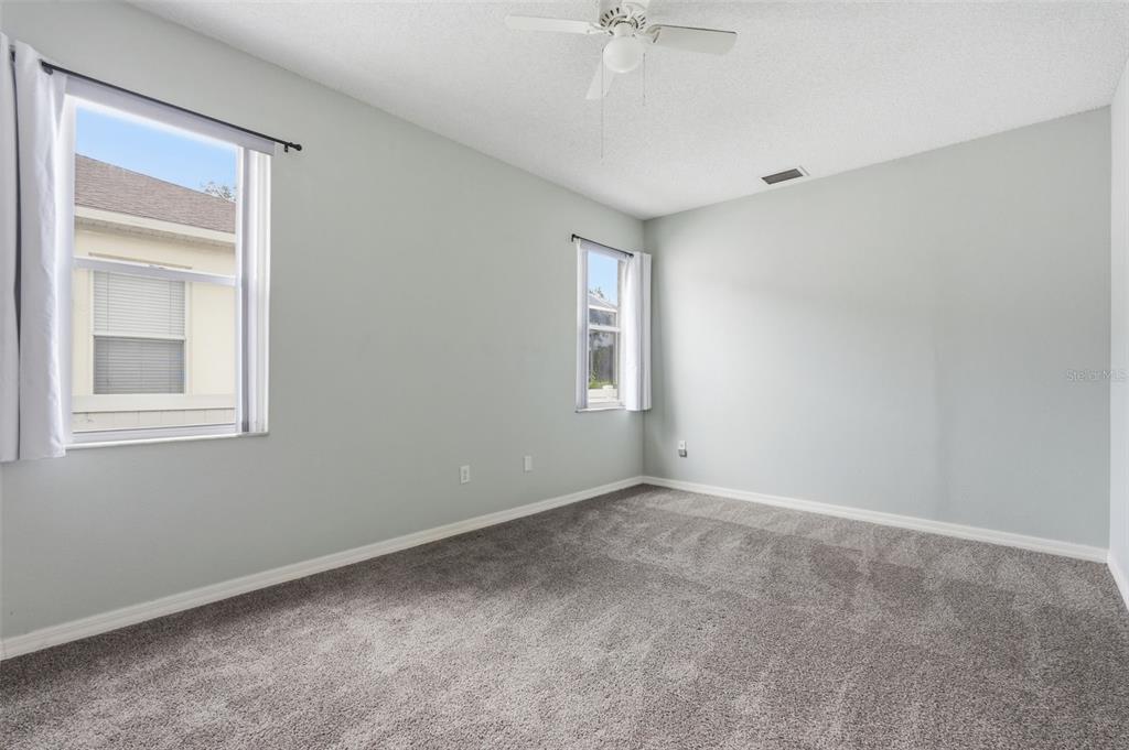 An empty bedroom features light gray walls, gray carpeting, a ceiling fan, and two windows — 11214 SAILBROOKE DRIVE, RIVERVIEW, FL