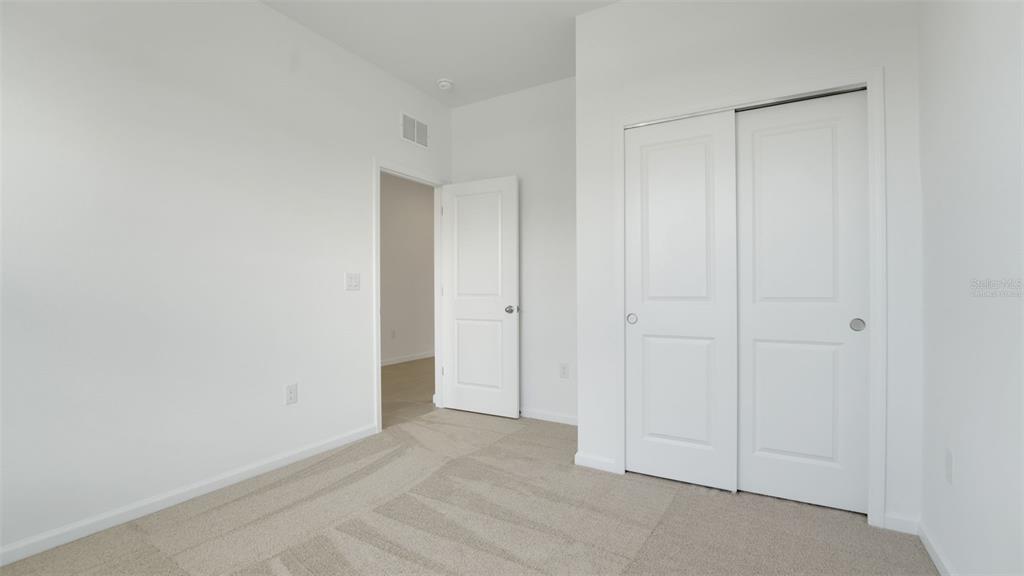 A bedroom features white walls, beige carpet, a closet with sliding doors, and an open doorway — 4094 PENELOPE AVENUE, LAKE WALES, FL