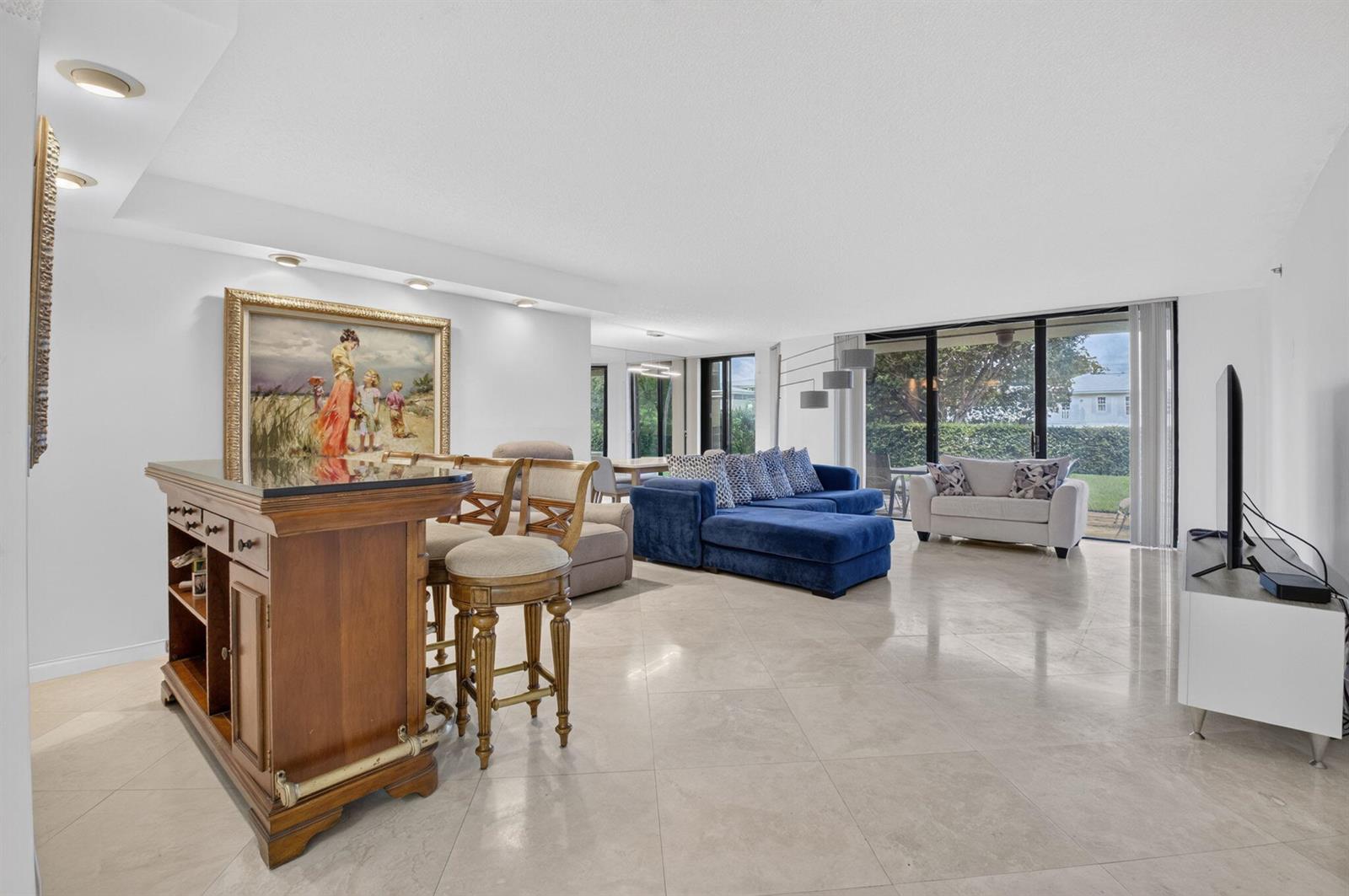 An open-concept living area features a wooden bar, blue sectional sofa, and light tile flooring — 1401 S Ocean Boulevard # 1060, Boca Raton FL 33432, BOCA RATON, FL