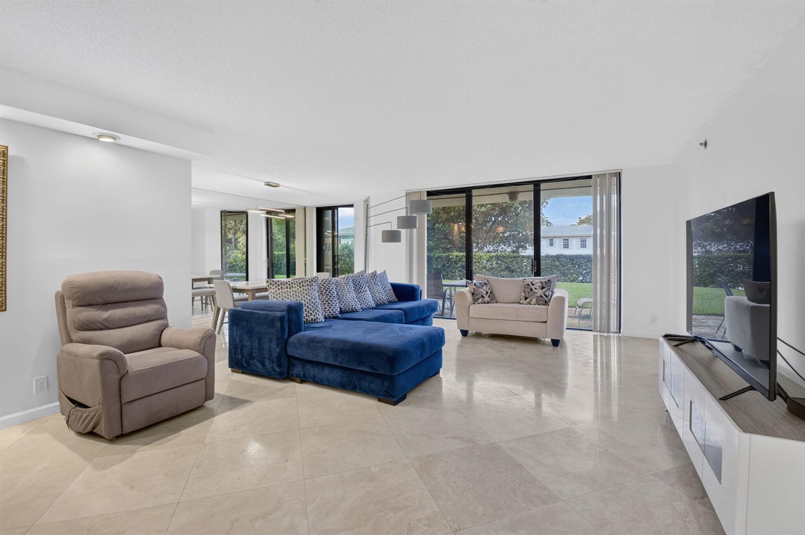 A living room features a blue sectional, a beige recliner, and a television on a stand — 1401 S Ocean Boulevard # 1060, Boca Raton FL 33432, BOCA RATON, FL