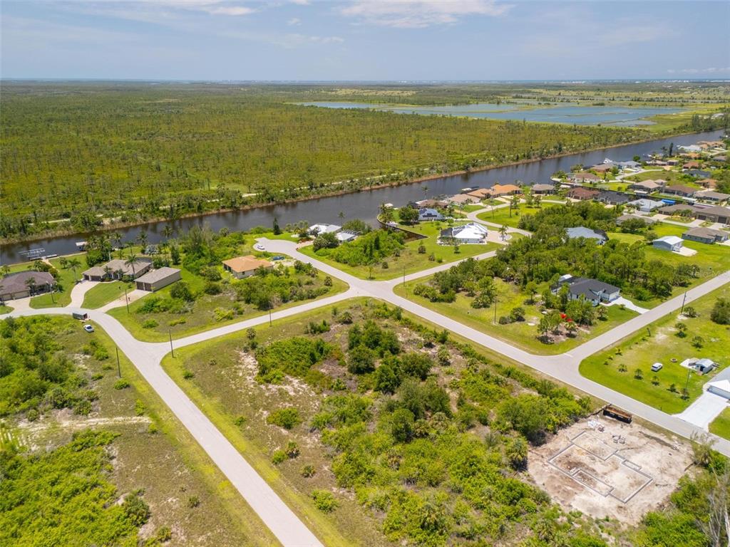 An aerial view shows a residential neighborhood with a canal, undeveloped lots, and scattered houses — 10536 ST PAUL DRIVE, PORT CHARLOTTE, FL