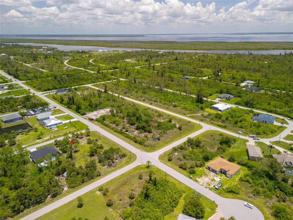 An aerial view shows a residential neighborhood with scattered houses, vacant lots, and a distant waterway — 10536 ST PAUL DRIVE, PORT CHARLOTTE, FL