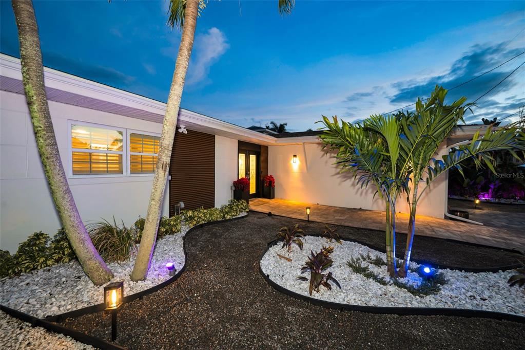 A modern house exterior features a gravel walkway, white stone landscaping, and palm trees at dusk — 16353 REDINGTON DRIVE, REDINGTON BEACH, FL