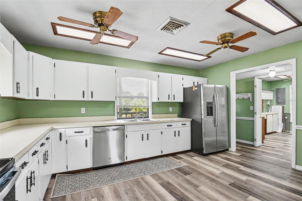A kitchen features white cabinets, stainless steel appliances, green walls, and wood-look flooring — 888 HARMONY LANE, ENGLEWOOD, FL