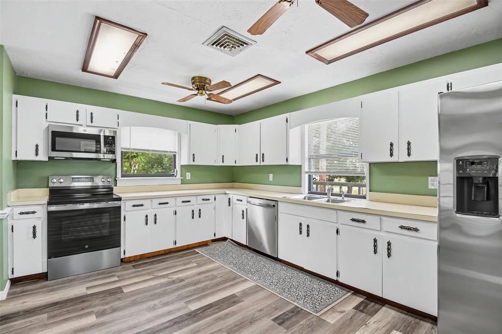 A kitchen features white cabinets, stainless steel appliances, green walls, and wood-look flooring — 888 HARMONY LANE, ENGLEWOOD, FL