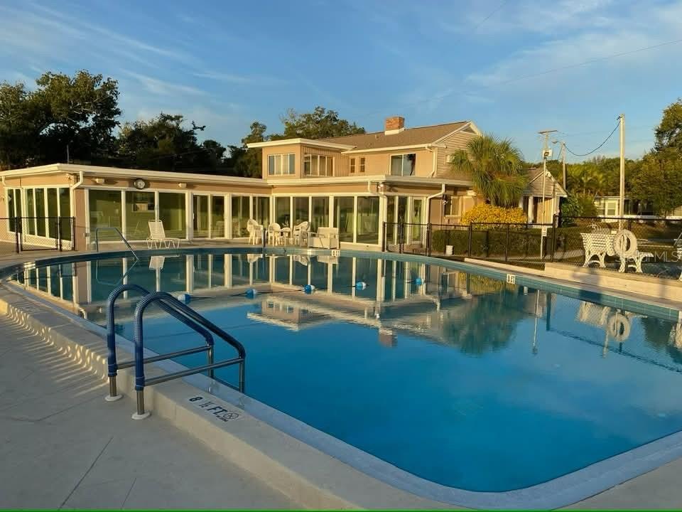 A large swimming pool sits in front of a two-story house with glass-enclosed patio areas — 585 SKY HARBOR DRIVE UNIT 126, CLEARWATER, FL