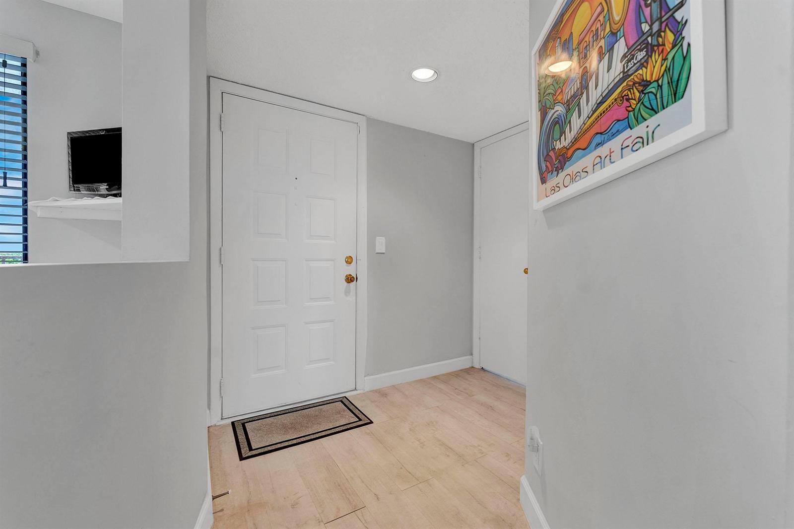 An entryway features a white door, light wood-look flooring, and a framed art print — 14475 Strathmore Lane # 703, Delray Beach FL 33446, DELRAY BEACH, FL