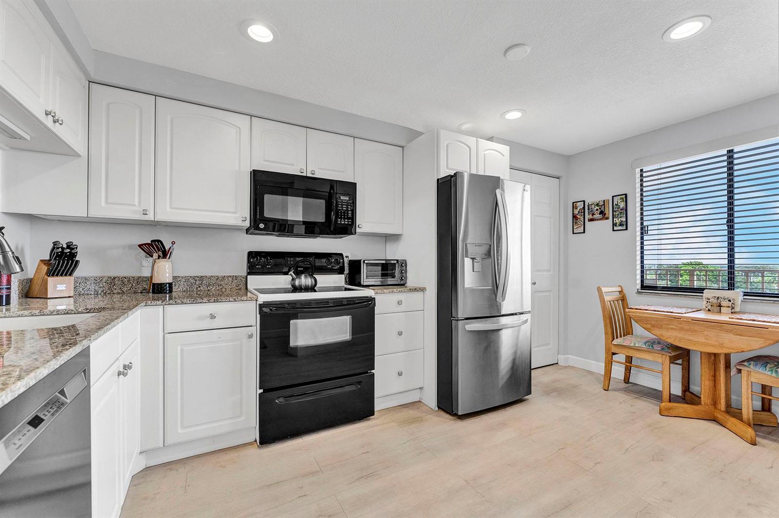 A kitchen with white cabinets, granite countertops, stainless steel appliances, and a small dining area — 14475 Strathmore Lane # 703, Delray Beach FL 33446, DELRAY BEACH, FL
