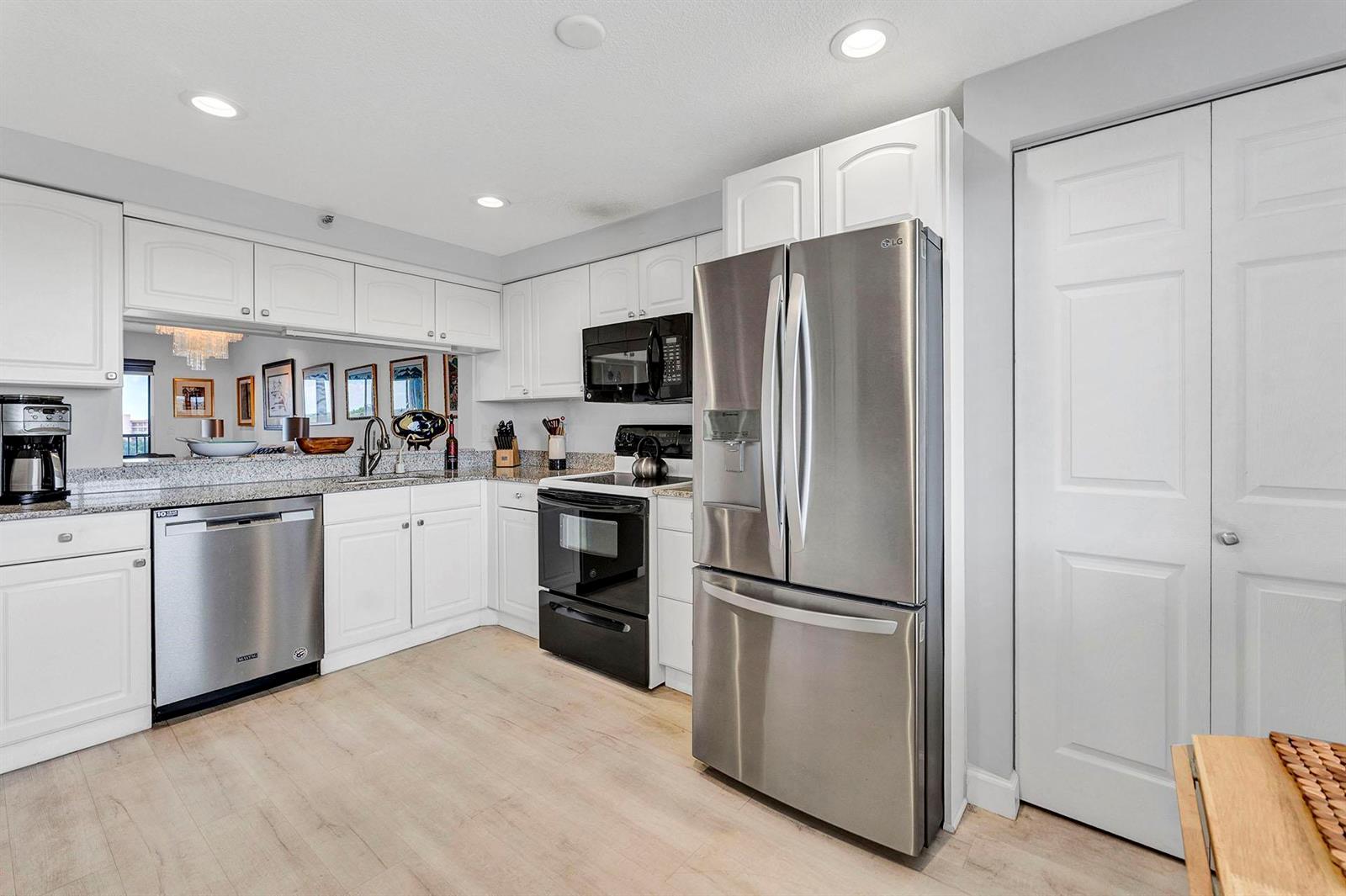 A kitchen features white cabinetry, stainless steel appliances, granite countertops, and light wood-look flooring — 14475 Strathmore Lane # 703, Delray Beach FL 33446, DELRAY BEACH, FL