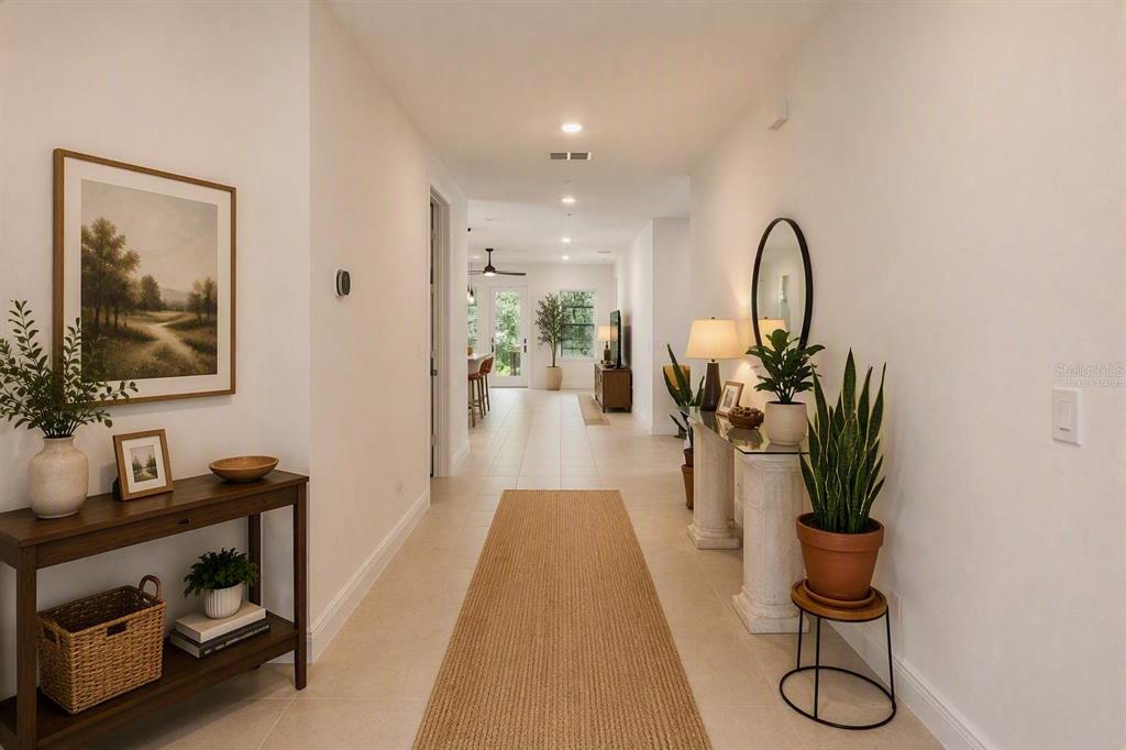 A long, bright hallway features tiled floors, a runner rug, and console tables with decor — 1699 MEADOWLARK DRIVE, DELTONA, FL