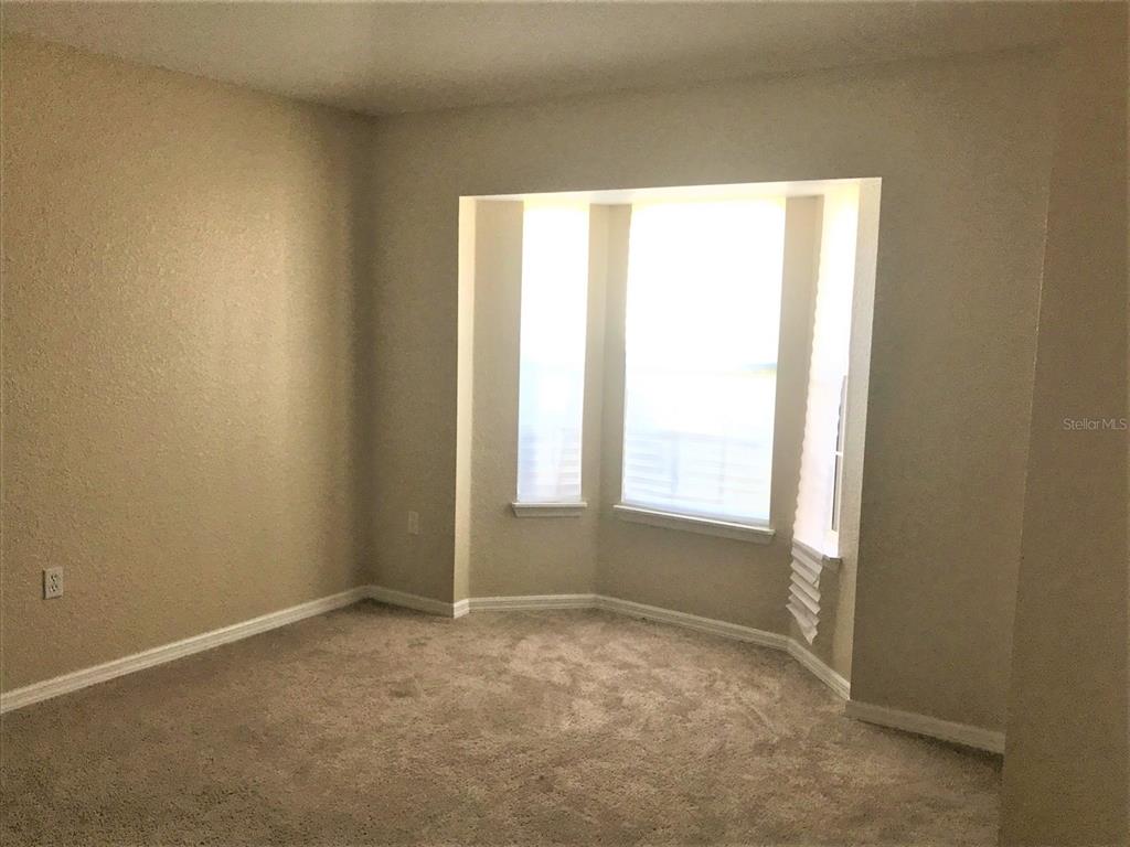 An empty room with beige walls, tan carpet, and a bay window — 3480 HAWKIN DRIVE, KISSIMMEE, FL