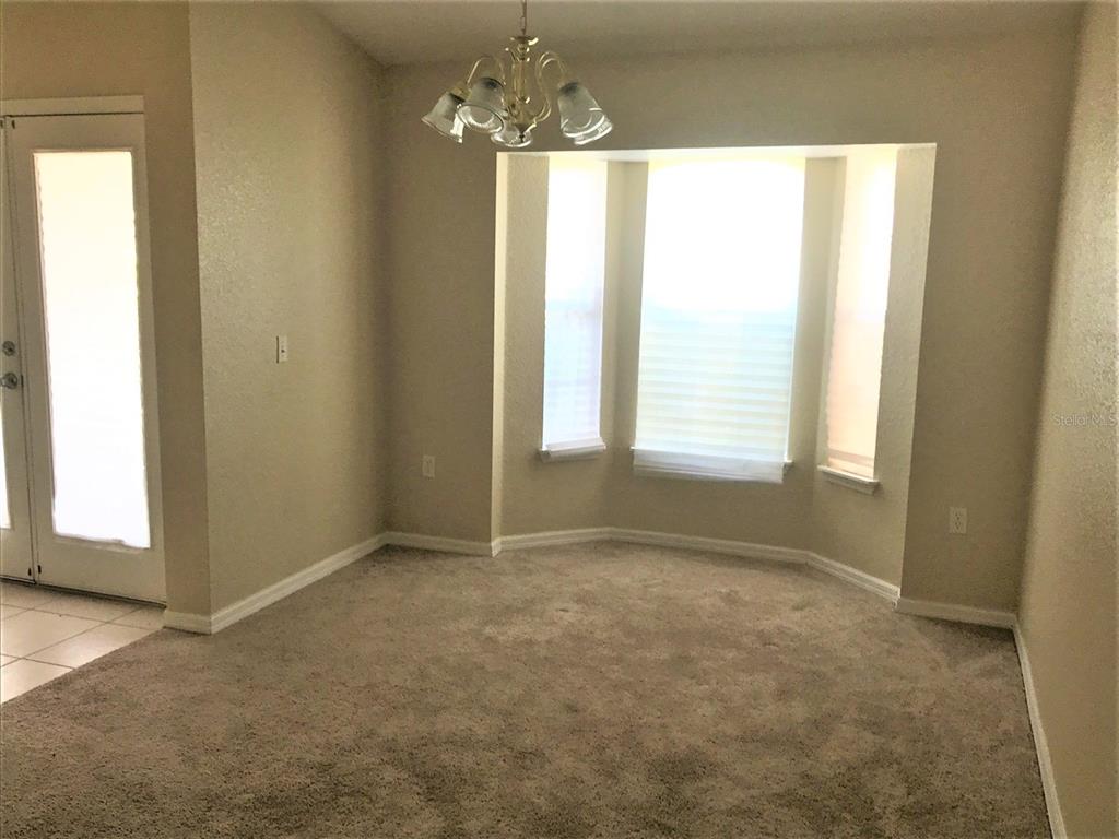 A dining area features beige carpet, a bay window, and a traditional chandelier — 3480 HAWKIN DRIVE, KISSIMMEE, FL