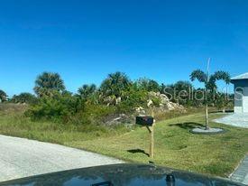 A vacant, grassy lot with scattered trees and shrubs is viewed from a paved road — 14272 AURELLA CIRCLE, PORT CHARLOTTE, FL