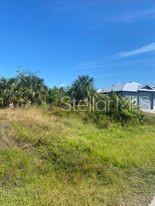 A vacant, grassy residential lot sits next to a modern house under a clear blue sky — 14272 AURELLA CIRCLE, PORT CHARLOTTE, FL