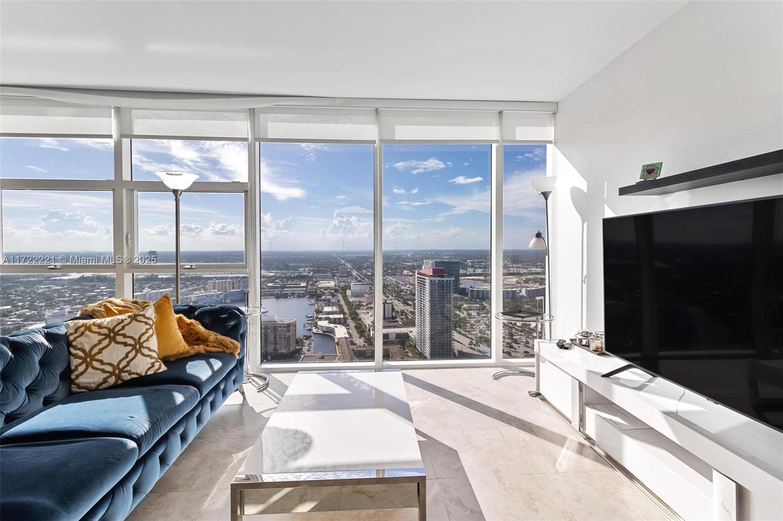 A living room features a blue tufted sofa, white coffee table, and floor-to-ceiling city views — 1830 S Ocean Dr # 4507, Hallandale Beach FL 33009, HALLANDALE BEACH, FL