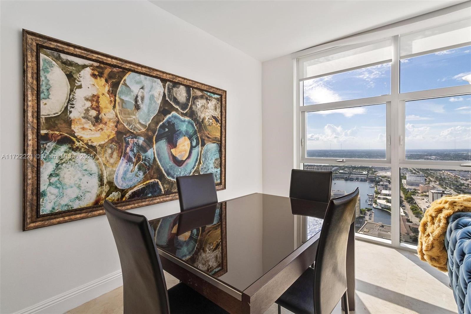A dining room features a dark glass table, four chairs, large wall art, and floor-to-ceiling windows — 1830 S Ocean Dr # 4507, Hallandale Beach FL 33009, HALLANDALE BEACH, FL