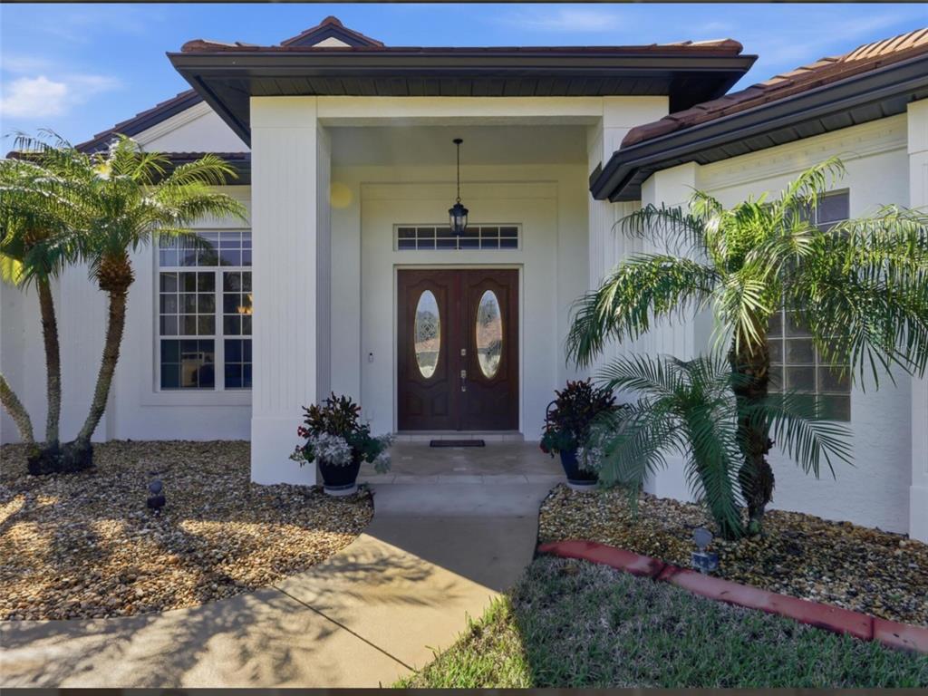 The front entrance of a house features double wooden doors, white columns, and palm trees — 4967 WILD DAISY LANE, VENICE, FL