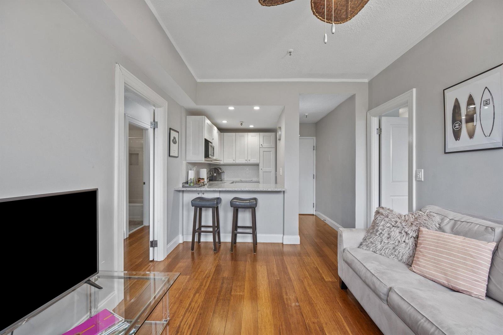 A living room with hardwood floors, a gray sofa, and an open kitchen with bar seating — 235 Sunrise Avenue # 3232, Palm Beach FL 33480, PALM BEACH, FL