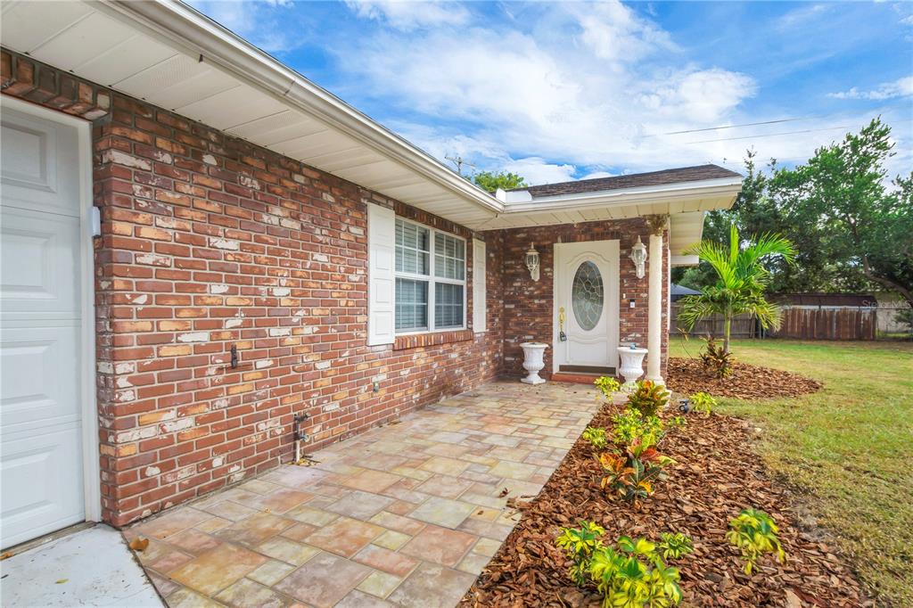 A brick house exterior features a stone-tiled front porch, a white door, and landscaping — 1206 SUSAN LANE, AUBURNDALE, FL