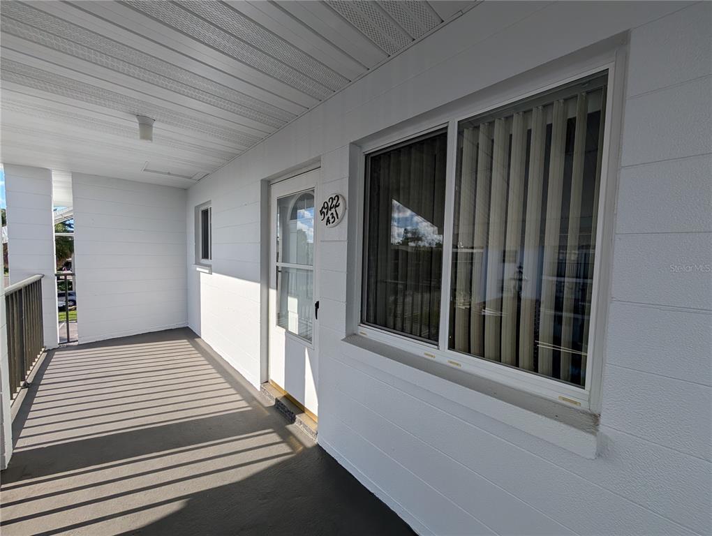 A covered exterior walkway leads to a white door and a window with vertical blinds — 5922 GARDEN LANE UNIT A31, BRADENTON, FL