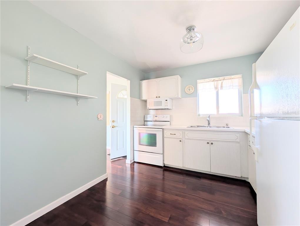 A kitchen with white cabinets, white appliances, light blue walls, and dark wood flooring — 5922 GARDEN LANE UNIT A31, BRADENTON, FL