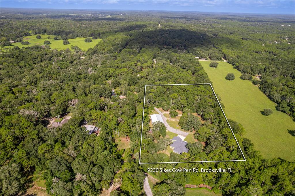 An aerial view shows a house and outbuilding on a wooded lot surrounded by fields — 9230 SIKES COW PEN ROAD, BROOKSVILLE, FL