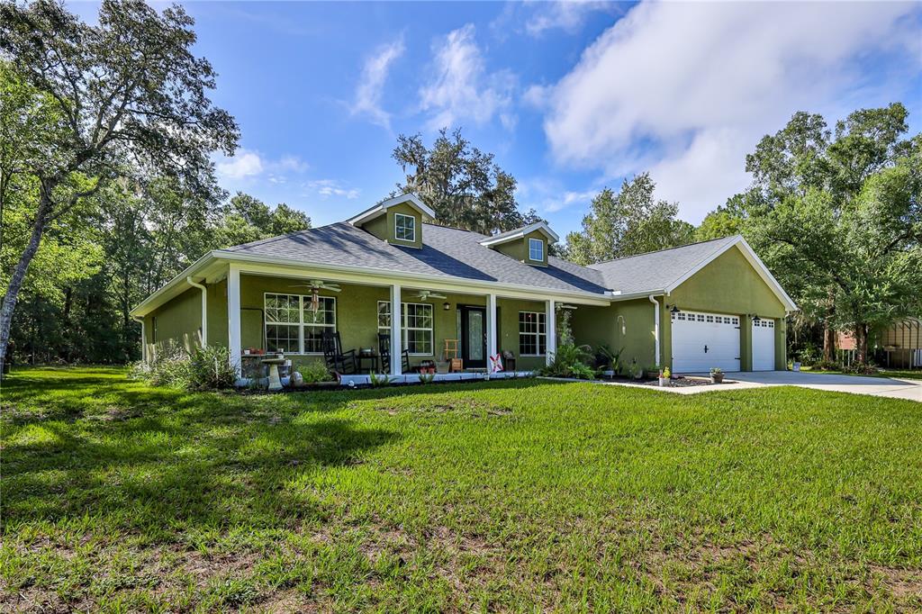 A single-story green house with a covered front porch, dormer windows, and an attached garage — 9230 SIKES COW PEN ROAD, BROOKSVILLE, FL