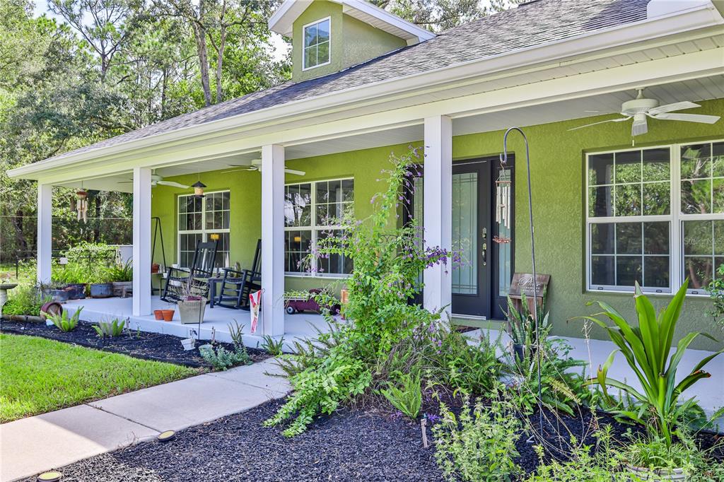 A lime green house features a covered front porch with rocking chairs and landscaping — 9230 SIKES COW PEN ROAD, BROOKSVILLE, FL
