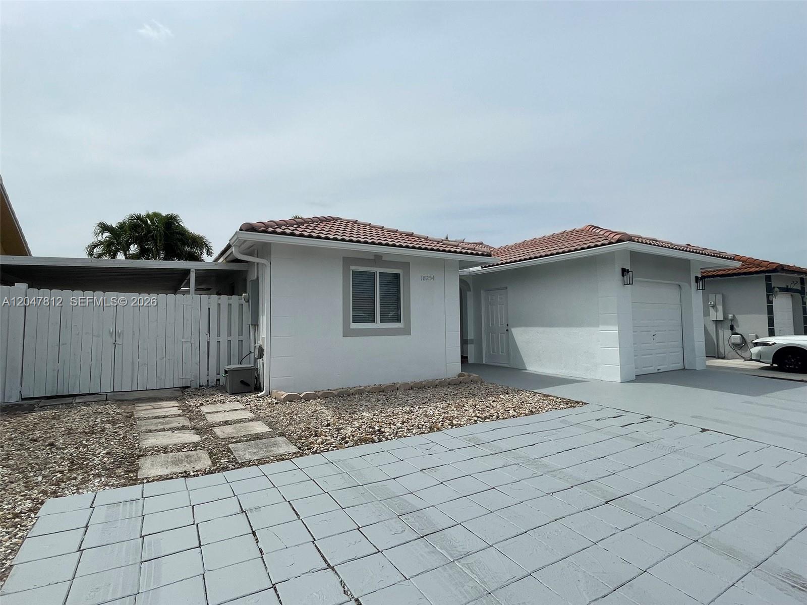 A white single-story house features a tiled roof, a garage, and a gravel front yard — 18254 SW 143rd Pl # 0, Miami FL 33177, MIAMI, FL