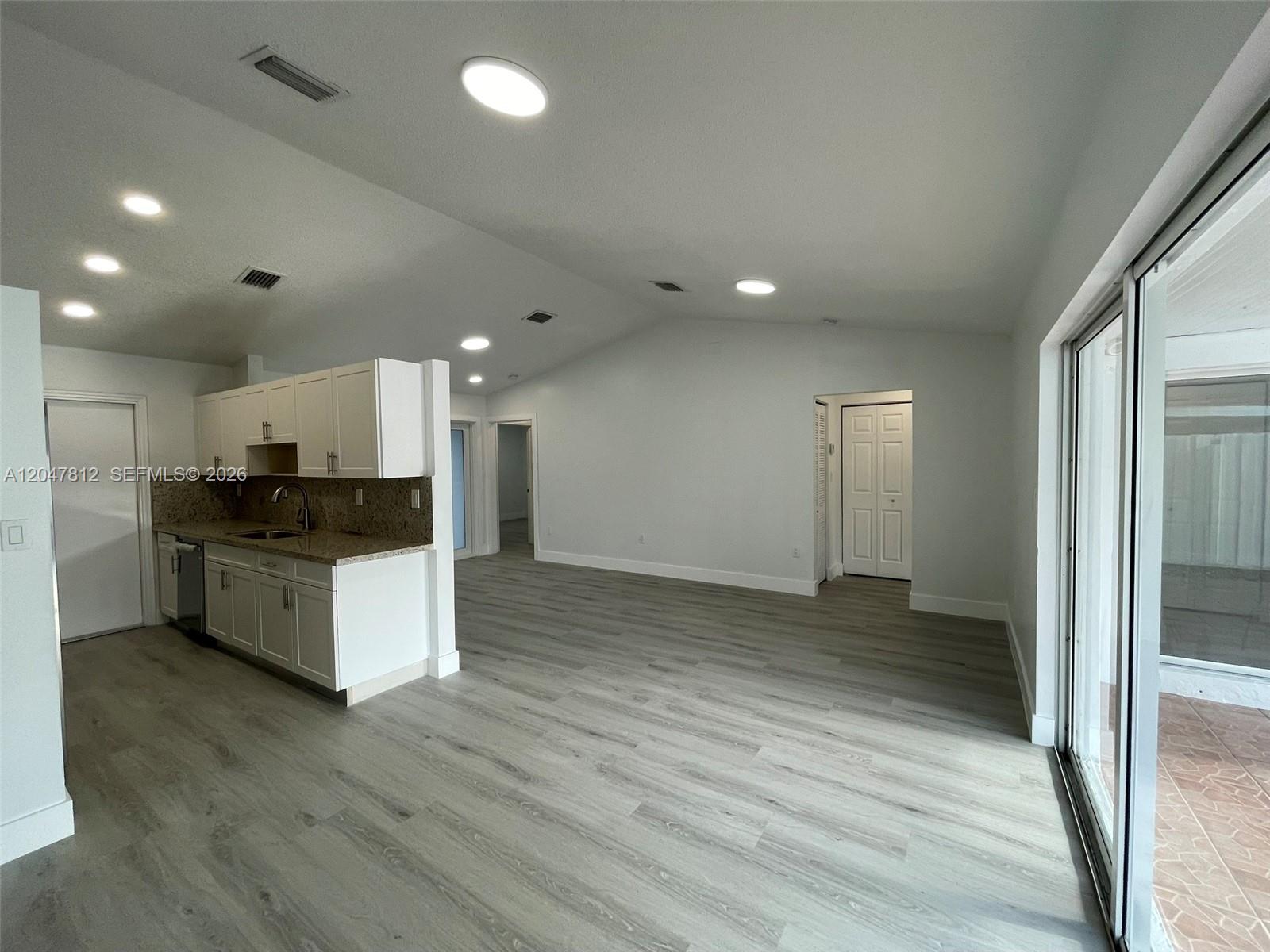 A kitchen with white cabinets and granite countertops opens into a spacious living area — 18254 SW 143rd Pl # 0, Miami FL 33177, MIAMI, FL