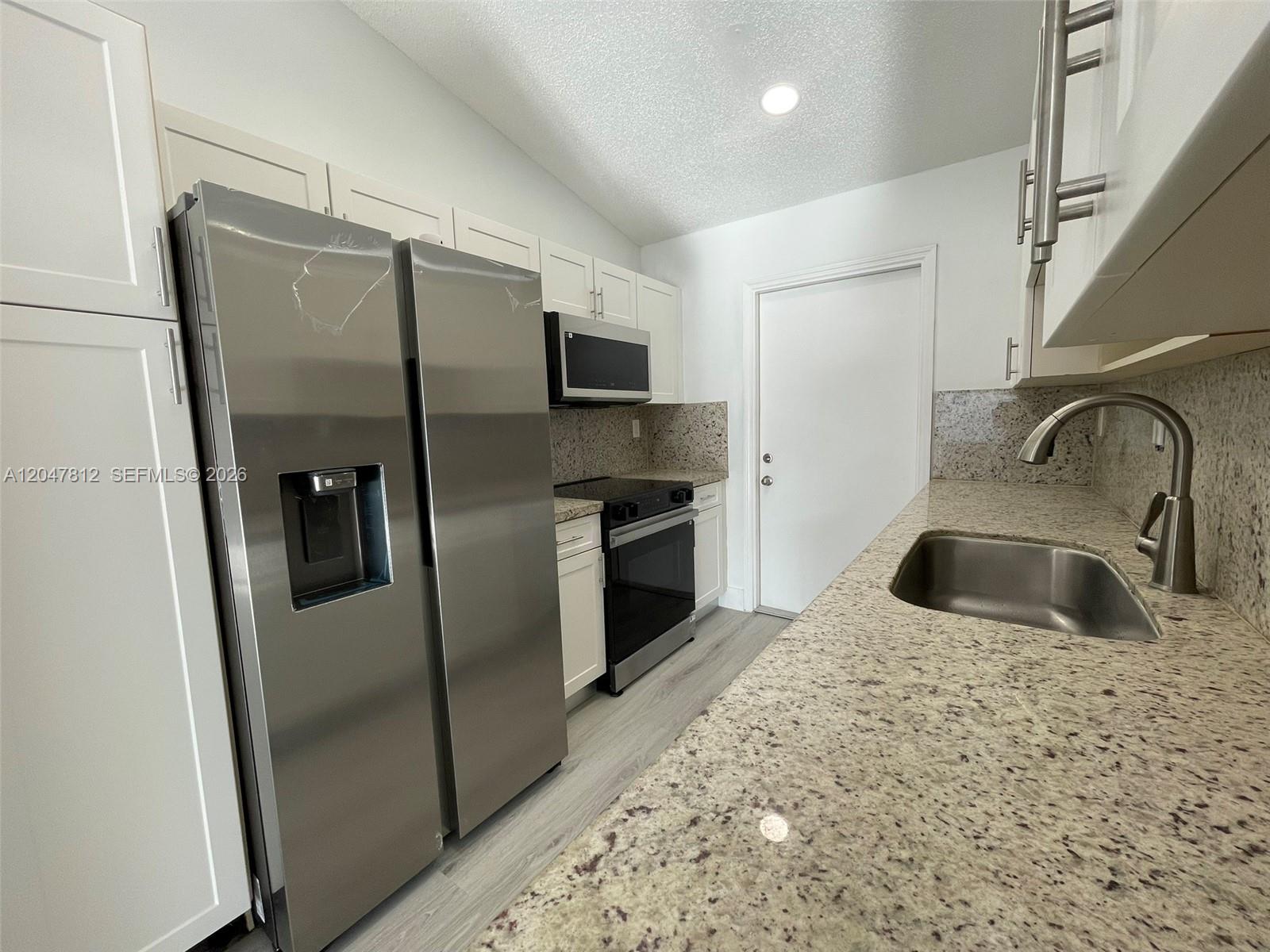 A kitchen features white cabinets, stainless steel appliances, and speckled granite countertops — 18254 SW 143rd Pl # 0, Miami FL 33177, MIAMI, FL