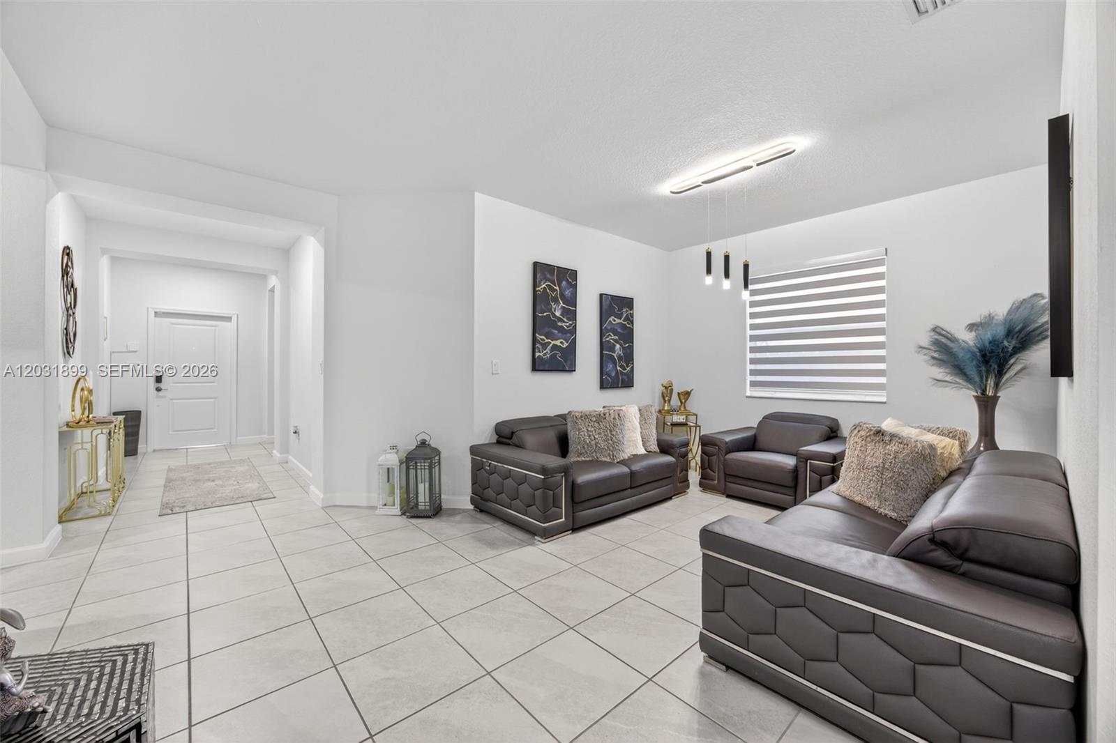 A living room features gray tile floors, dark leather furniture, and two abstract wall paintings — 21363 SW 127th Ct, Miami FL 33177, MIAMI, FL